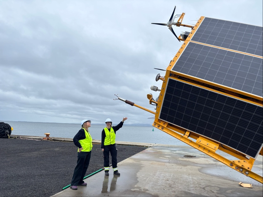 Two workers in safety vests and helmets inspecting large solar panels near water